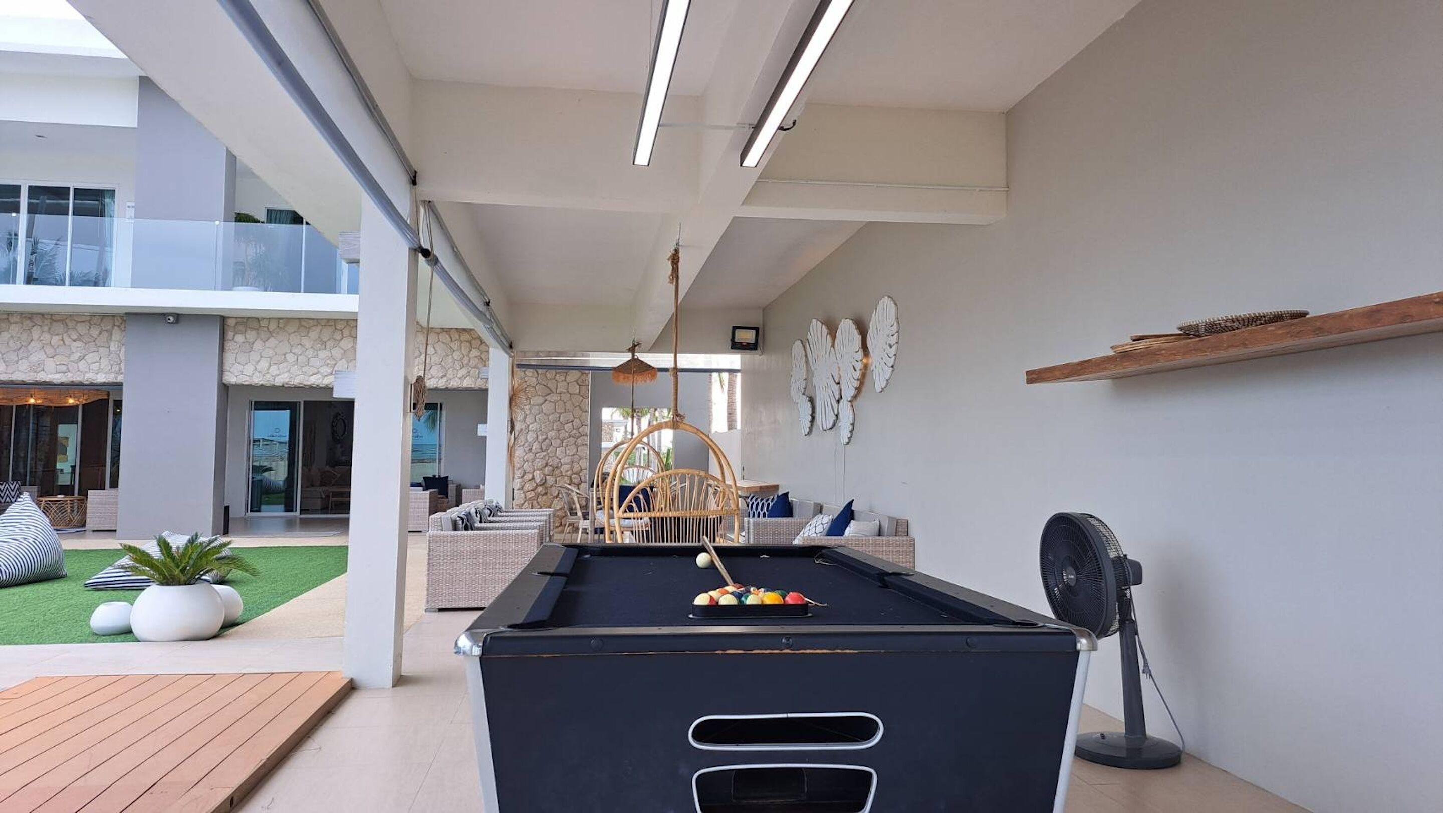 A modern indoor pool area with a pool table, lounge seating, and a view of the outdoor patio.