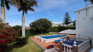 Ein Garten mit Pool, einer Terrasse mit blauen Liegestühlen und einem weißen Gebäude mit Satellitenschüssel.