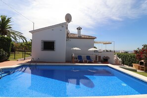 A swimming pool with a white building in the background, a satellite dish, and a clear sky.