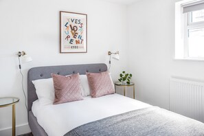A neatly arranged bedroom with a bed, bedside lamps, a small table, and a framed poster on the wall.