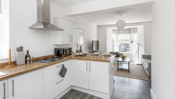 A modern kitchen with white cabinets, a stainless steel range hood, and a wooden countertop. - Stylish Apartment In Leafy Central Neighbourhood (Cardiff)