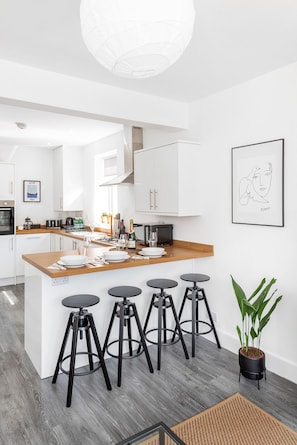 A modern kitchen with a central island, bar stools, a potted plant, and artwork on the walls.