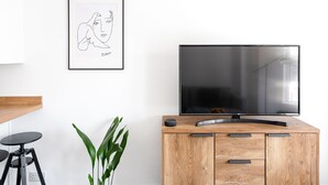 A modern living room with a wooden cabinet, a flat-screen TV, a framed artwork, and a potted plant. - Stylish Apartment In Leafy Central Neighbourhood (Cardiff)