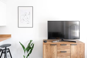 Relax and unwind in this stylish space, featuring a large flat-screen TV, a framed artwork, and a cozy seating area with a potted plant.