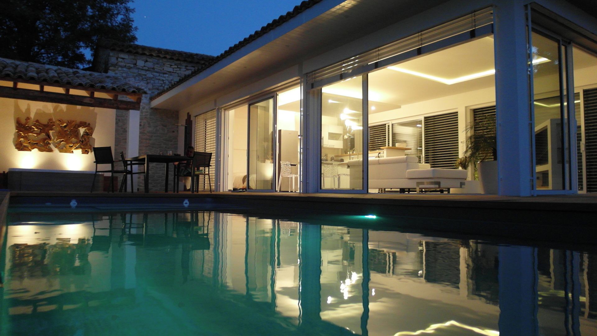 A modern house with a swimming pool, large glass doors leading to a living area, and a stone wall.