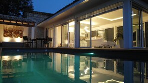 A modern house with a swimming pool, large glass doors leading to a living area, and a stone wall.