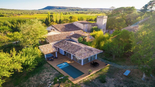 A villa with a swimming pool, surrounded by lush greenery and a stone tower.