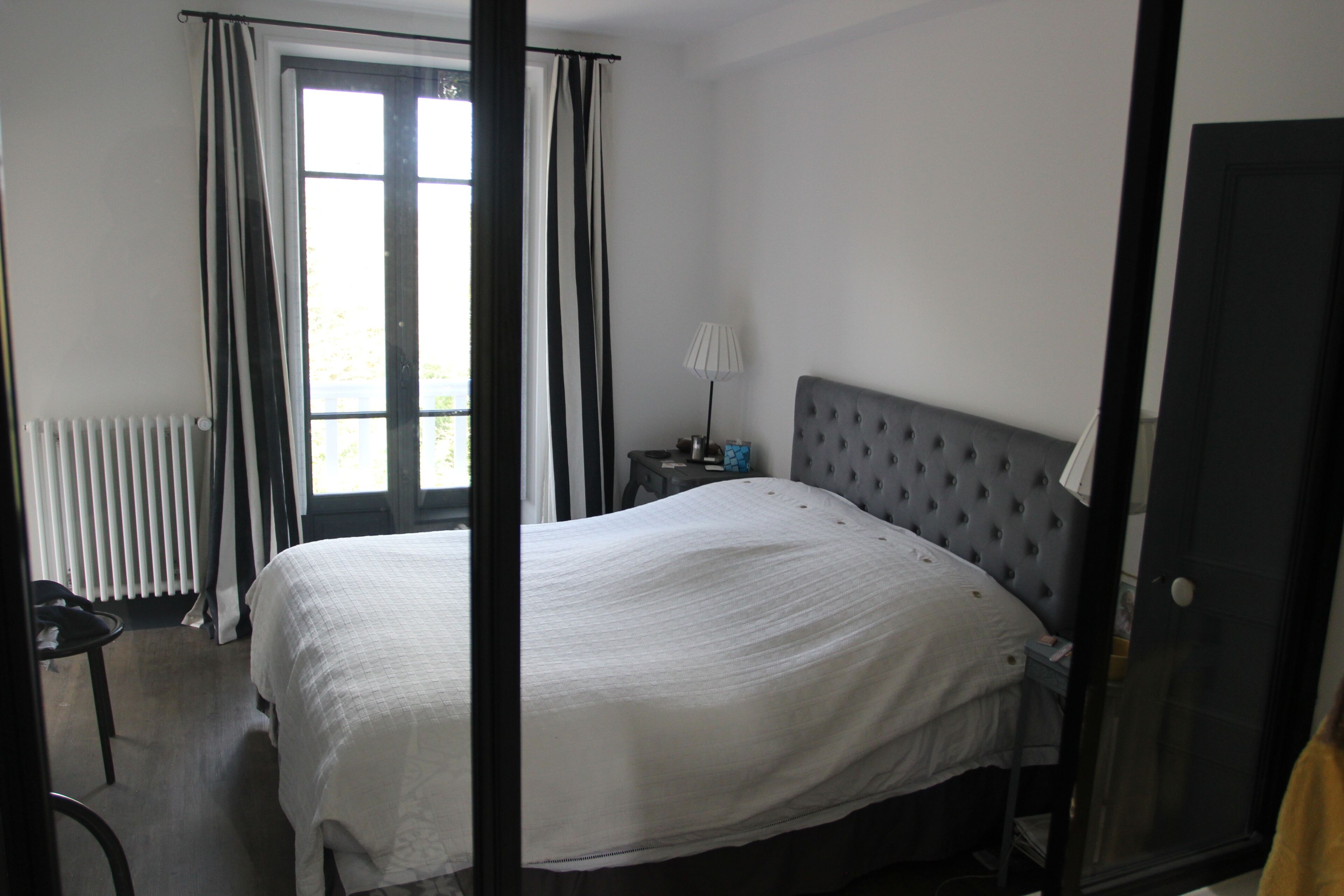 Une chambre avec un grand lit, un radiateur, une fenêtre avec des rideaux et une table de chevet avec une lampe.