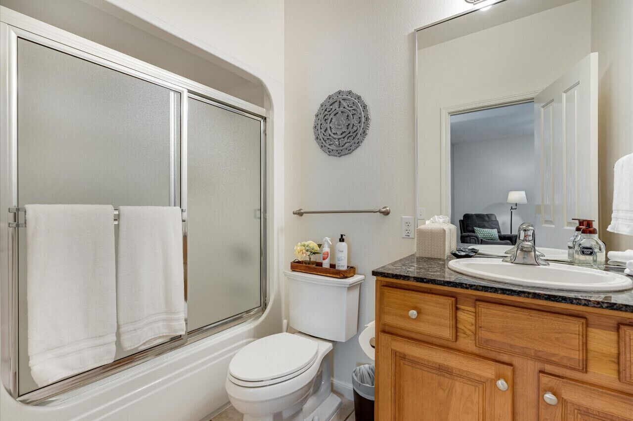 A bathroom with a glass shower enclosure, a toilet, a sink with a vanity, and a decorative wall piece.