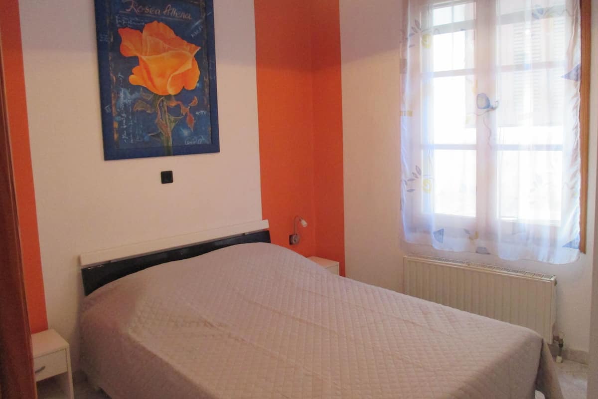 Ein Schlafzimmer mit einem Einzelbett, einem Fenster mit transparenten Vorhängen und einem Poster an der Wand.