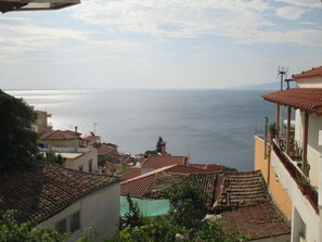 Uma vila costeira com edifícios de telhados em tons de terracota, vista para o mar e céu claro.