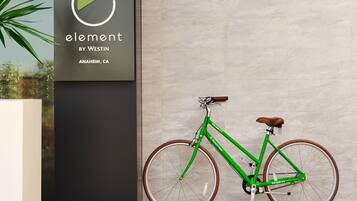 Een groene fiets met een bruin zadel en houten wielen, geparkeerd tegen een muur met een bord waarop staat: 'element by Westin, Anaheim, CA'.