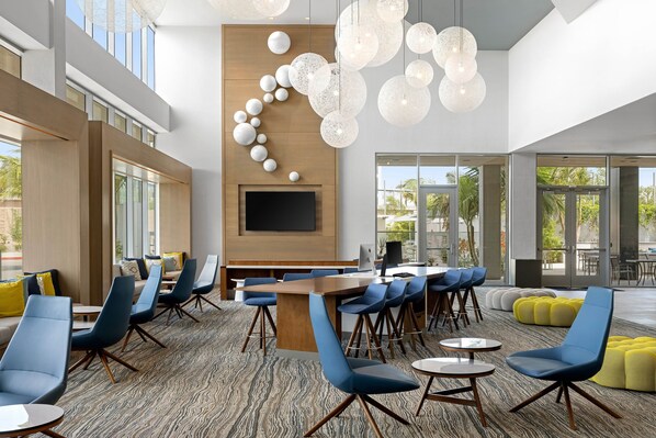 A modern lounge area with a long table, blue chairs, and a large screen. - Element by Marriott Anaheim Resort Convention Center (Anaheim)