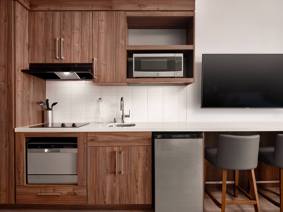 Una cucina moderna con mobili in legno, un forno a microonde integrato, una lavastoviglie e una TV a schermo piatto montata a parete.