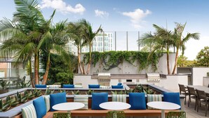 Eine Außenpatio-Terrasse mit Sitzgelegenheiten, einem Grill und Palmen.