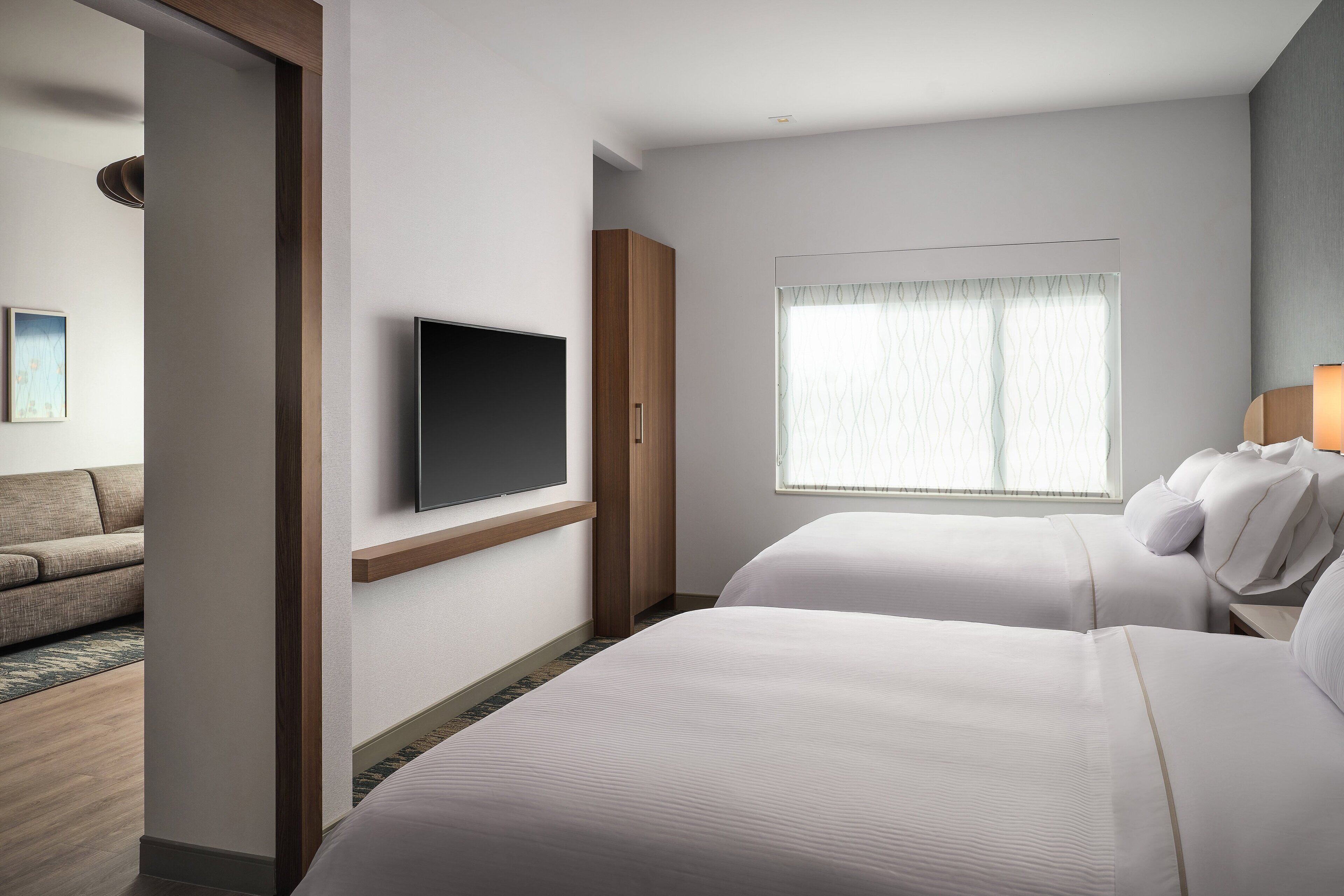 Habitación de hotel con dos camas, televisión, ventana con cortinas, sofá y un armario de madera.