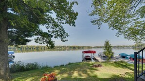 A lakeside deck with a picnic table, a covered area, and boats in the background. - Pet Friendly  w/ Private Dock - Steps to Rice Lake (Rice Lake)