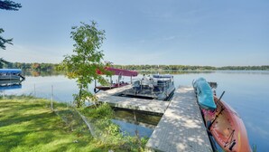 A dock with a kayak, a covered seating area, and a boat on a calm lake. - Pet Friendly  w/ Private Dock - Steps to Rice Lake (Rice Lake)