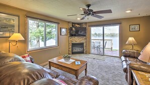 A living room with a fireplace, leather couches, a ceiling fan, and large windows. - Pet Friendly  w/ Private Dock - Steps to Rice Lake (Rice Lake)