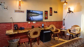 Eine gemütliche Bar mit einer Holztheke, Korbstühlen und einem großen Fernseher, der eine friedliche Seenlandschaft zeigt.