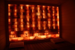 A sauna with a wooden bench and a wall of heated stones. - Boutiquehotel Freizeittempel (Wiener Neustadt)