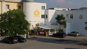 Un hôtel de charme, reconnaissable à son enseigne bien visible, avec des voitures garées devant et un ciel dégagé.
