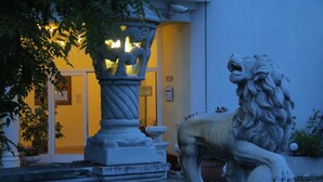 Une statue de lion en pierre se trouve dans une cour, avec l’entrée d’un bâtiment en arrière-plan.
