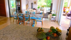 Un salón amplio con una mesa de comedor, sillas y un frutero.