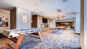 A modern hotel room with a foosball table, a TV, and a seating area with a patterned carpet. - Luxury 1BR | Health Club | Pool | Near PATH (Jersey City)