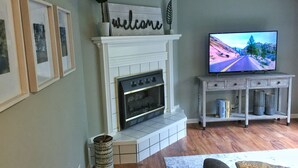 A living room with a fireplace, a television, framed pictures, and a decorative welcome sign. - "NEW" Designed for Comfort and Relaxation and close to everything! (Hot Springs)