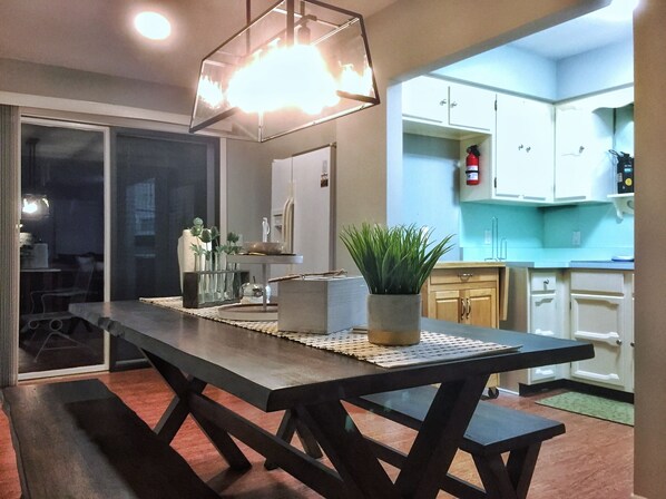 A modern kitchen with white cabinets, a wooden dining table, and a potted plant.