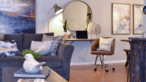 A modern living room with a grey sofa, a coffee table with a decorative bird, a desk with a laptop, and a chair with a pillow labeled "Arkansas." - "NEW" Designed for Comfort and Relaxation and close to everything! (Hot Springs)