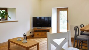 Una sala de estar con televisión, muebles de madera, una pequeña mesa con una taza y una planta en maceta.