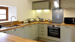 Cocina moderna con armarios grises claros, encimera de madera, campana extractora de acero inoxidable, microondas negro y horno empotrado.