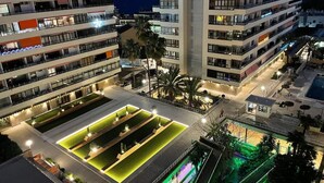Un hôtel à plusieurs étages doté de balcons, d’un espace piscine éclairé de lumières vertes et d’un petit bâtiment sur lequel est apposée une enseigne.