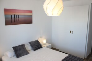 A bedroom with a bed, two pillows, a nightstand with a lamp, a wall-mounted painting, and a wardrobe.