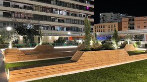 Un espace extérieur moderne, doté de bancs en bois et d’une pelouse artificielle, entouré d’immeubles avec des balcons et des fenêtres illuminées.