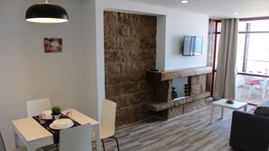 Un salon moderne avec une cheminée en pierre, un coin repas avec des meubles blancs et un téléviseur fixé au mur.