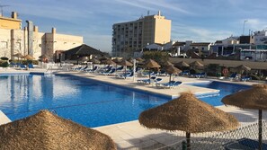 A swimming pool with lounge chairs and thatched umbrellas, surrounded by buildings.