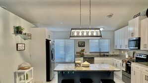 A modern kitchen with white cabinets, a marble countertop, and a central island with stools. - Pool home near Disney parks. (Kissimmee)
