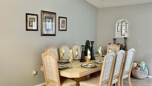A dining room with a wooden table set for six, surrounded by six chairs with cushioned seats. - Pool home near Disney parks. (Kissimmee)