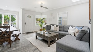 Una sala de estar moderna con un sofá gris, una mesa de centro de madera y un comedor con una mesa y sillas de madera.