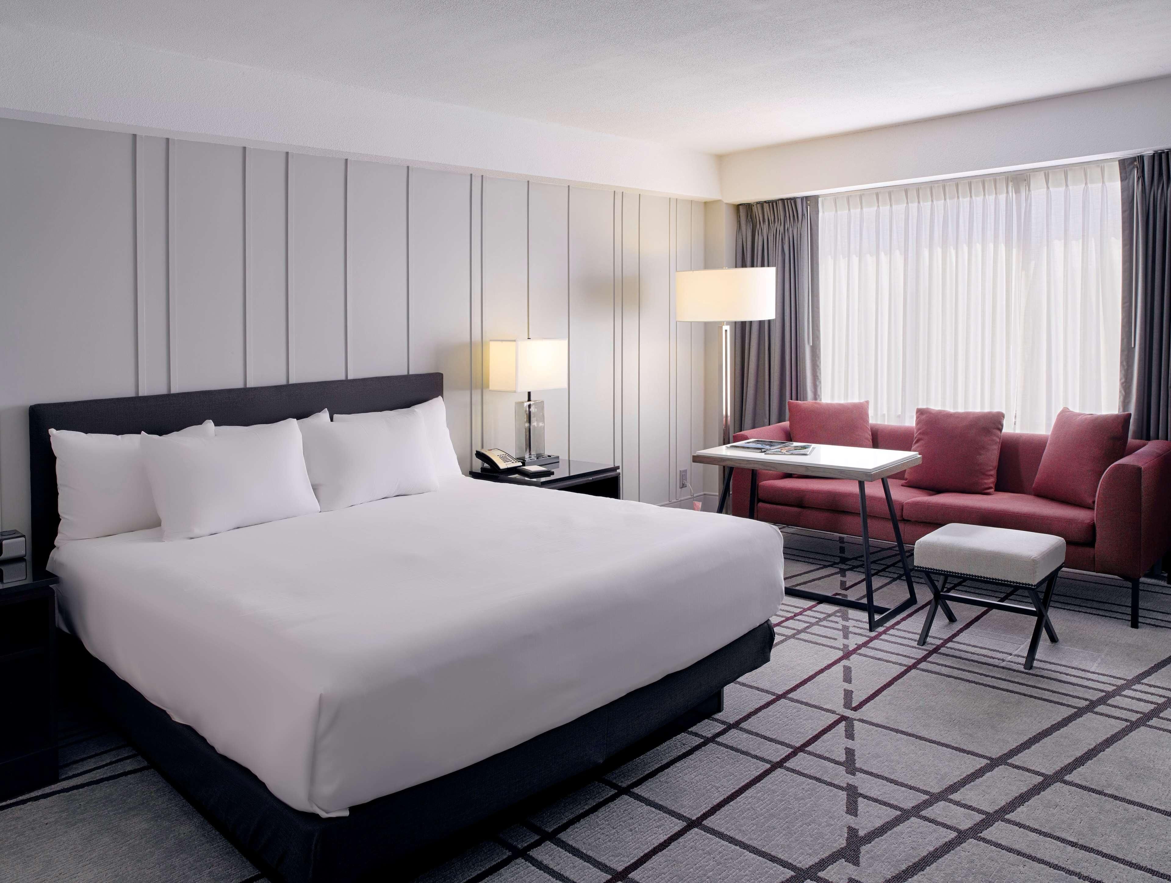 Ein Hotelzimmer mit einem großen Bett, einem Schreibtisch mit Lampe, einem roten Sofa und einem kleinen Tisch.