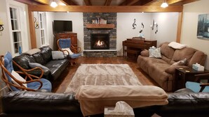A cozy living room with a fireplace, leather sofas, a piano, and a stone wall. - Spacious! Recent Remodel! 6 Min. to Raystown Lake! Linens&Towels provided! (Saxton)