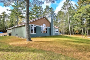 A two-story house with a green exterior and a brown roof, surrounded by a wooded area.