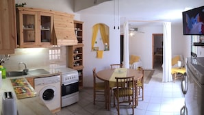 Une cuisine compacte avec des meubles en bois, un lave-linge, une cuisinière et un coin repas comprenant une table et des chaises.