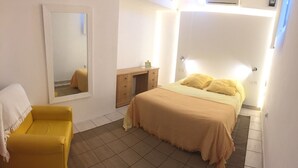 Une chambre à coucher avec un lit, une table de chevet, un miroir et un fauteuil jaune.