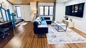 Una sala de estar moderna con techo de madera, un televisor grande, un sofá, una mesa de centro y una escalera con barandales azules.