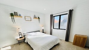 Un dormitorio ordenado con cama, lámparas de noche, un radiador y una ventana con cortinas.