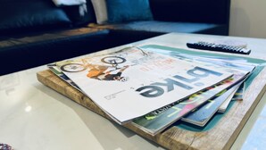 Una sala de estar con un sofá, una mesa de centro con revistas y un control remoto.